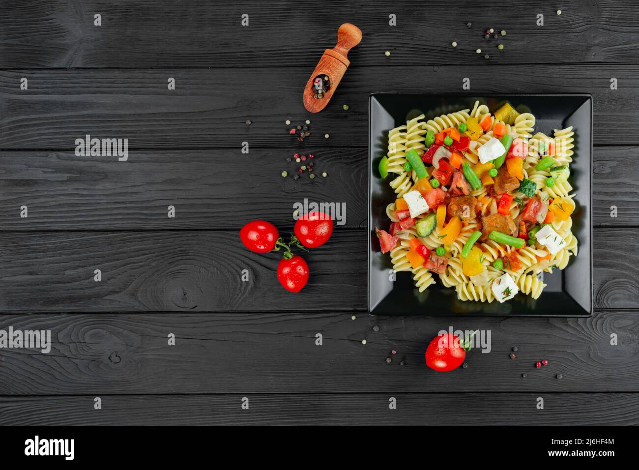 Pâtes Penne aux légumes, petits pois, poivrons, tomates, sauce, mozzarella sur fond de bois noir. Pâtes italiennes avec légumes et sp Banque D'Images