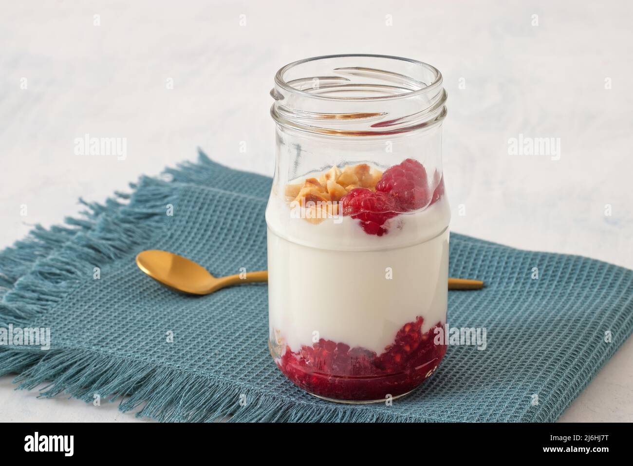 Alimentation saine, yaourt grec ordinaire, framboises fraîches et noisettes écrasées sur fond blanc. Banque D'Images