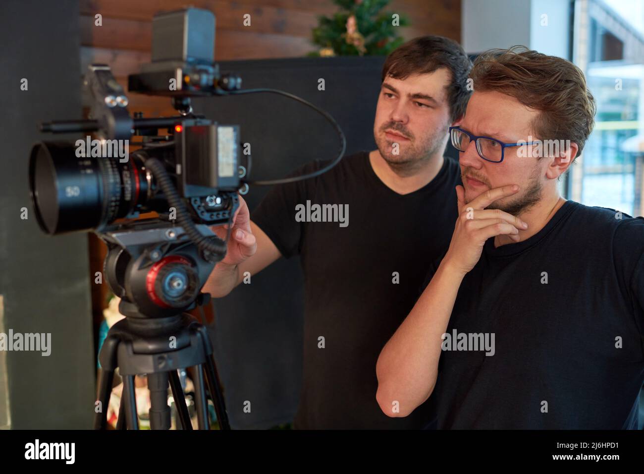 Jeune vidéaste ou opérateur pensif et son assistant de réglage de caméra vidéo tout en préparant le tournage de publicité Banque D'Images