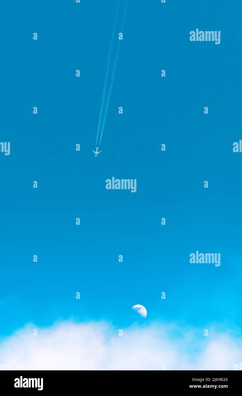 Avion voyageant à travers le ciel bleu avec la lune et les nuages, vue en angle bas Banque D'Images