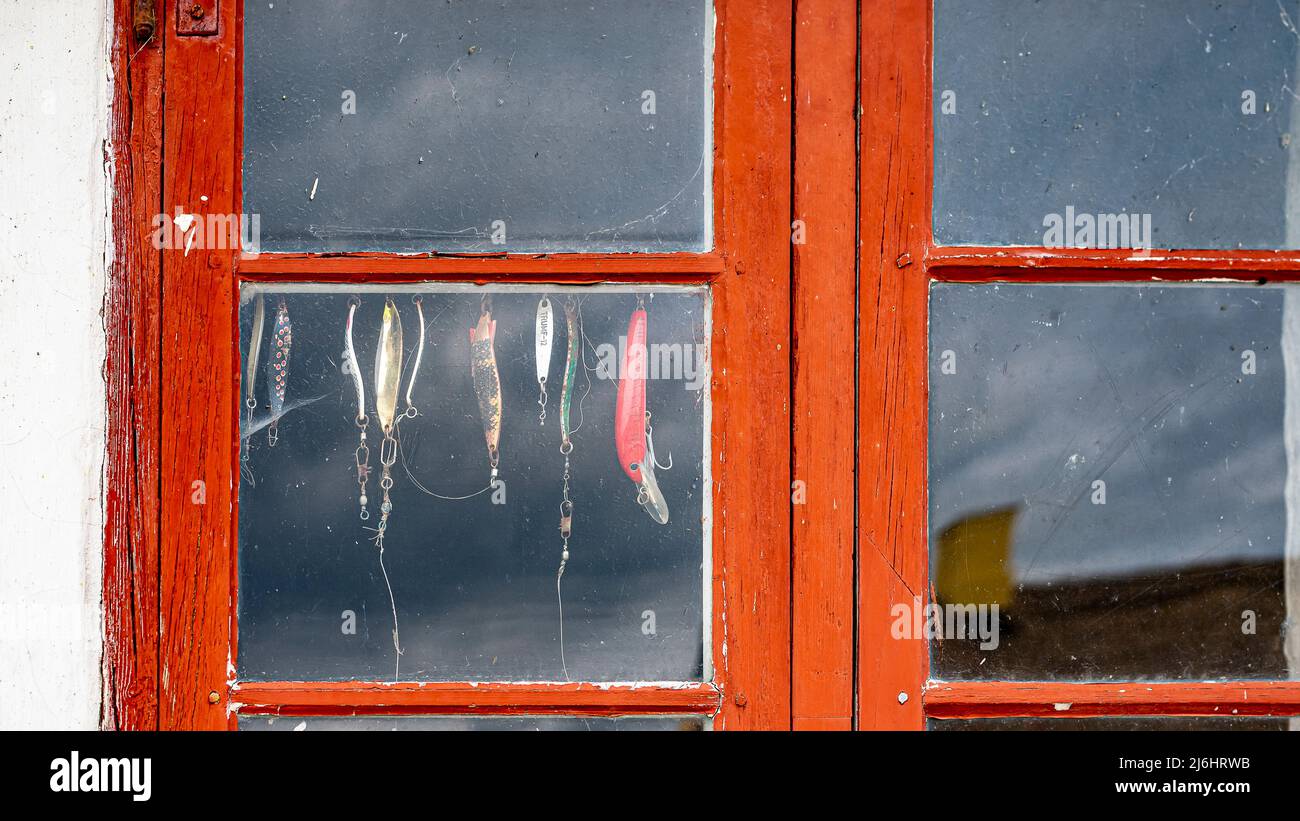 Leurres tournants suspendus dans une fenêtre rouge sur une ancienne cabane de pêche, Jyllinge, Danemark, 1 mai 2022 Banque D'Images