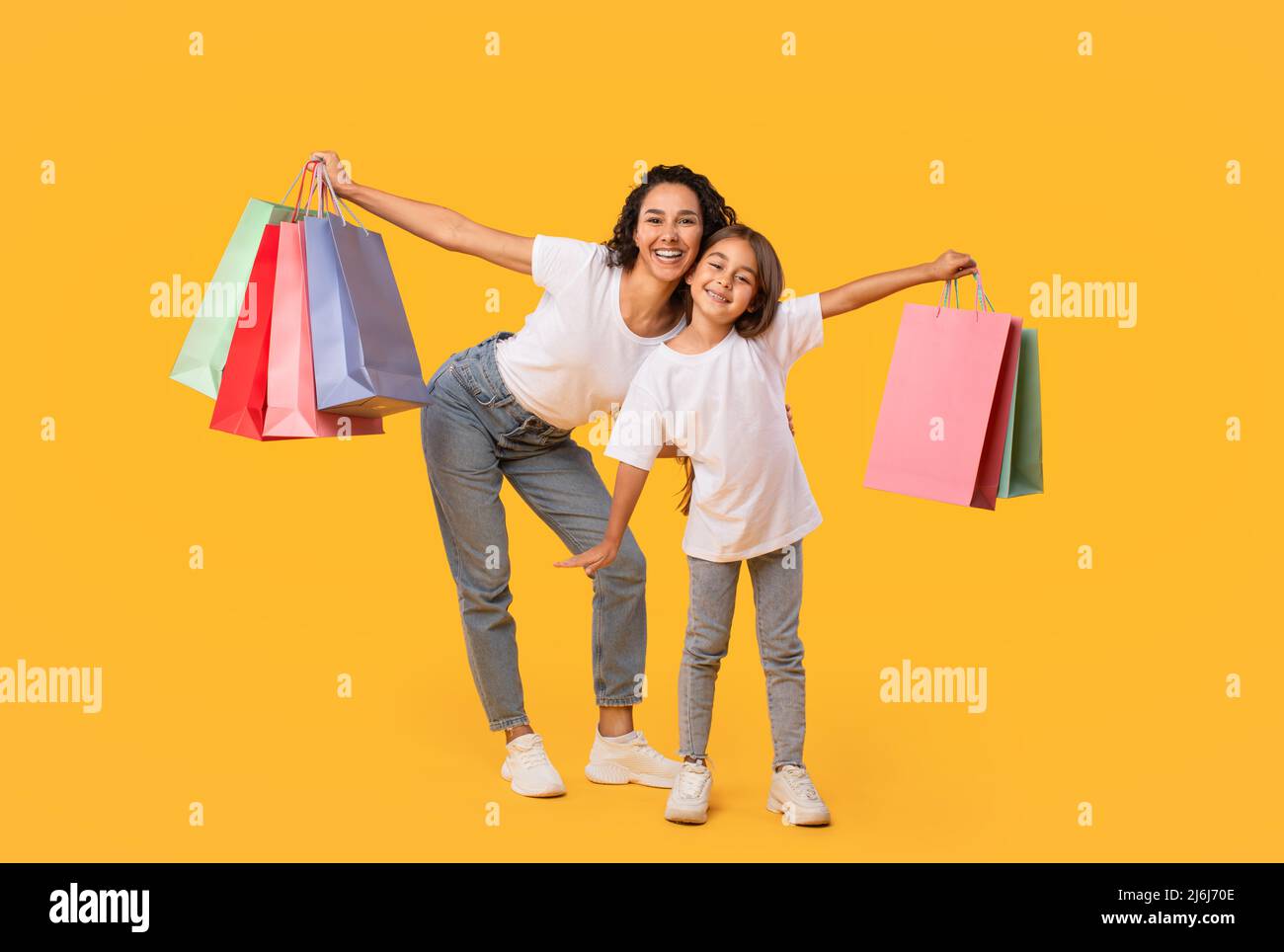 Maman arabe et fille posant tenant des sacs d'achats, fond jaune Banque D'Images