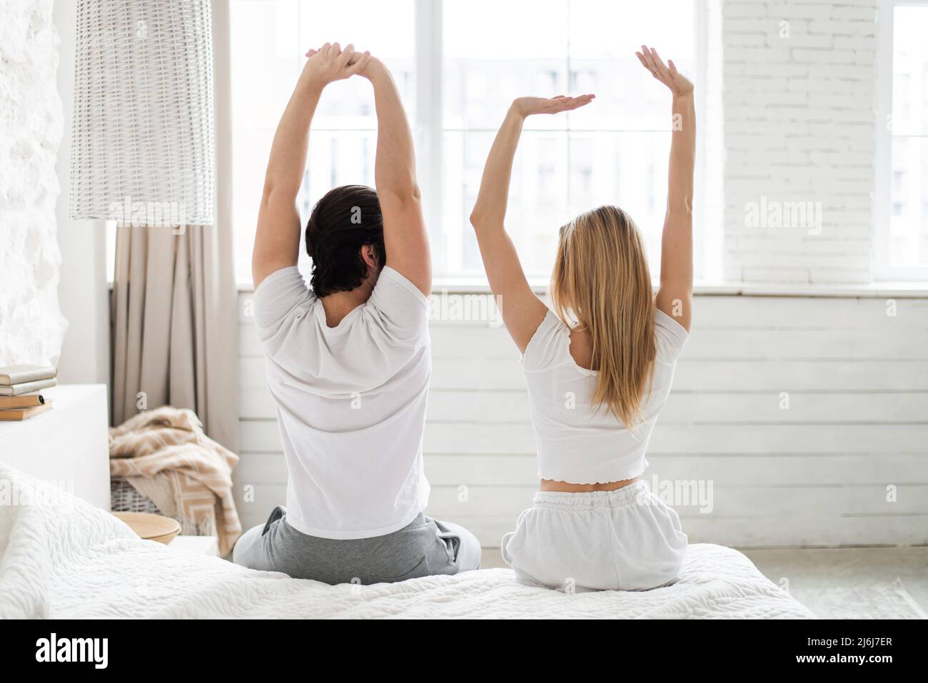 Vue arrière d'un jeune couple qui s'étire sur le lit après s'être réveillé à la maison Banque D'Images