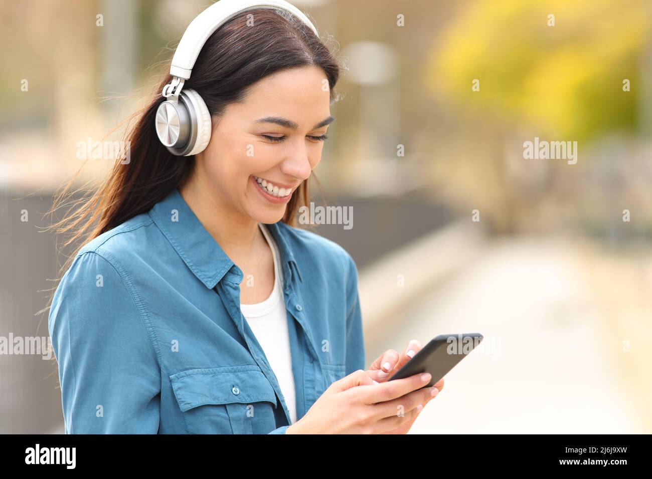 Une femme heureuse qui porte un casque écoute de la musique ou regarde des fichiers multimédias sur un smartphone dans un parc Banque D'Images