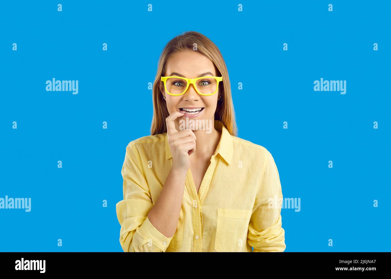 Portrait de la bonne drôle curieuse étudiante fille en lunettes sur fond bleu studio Banque D'Images