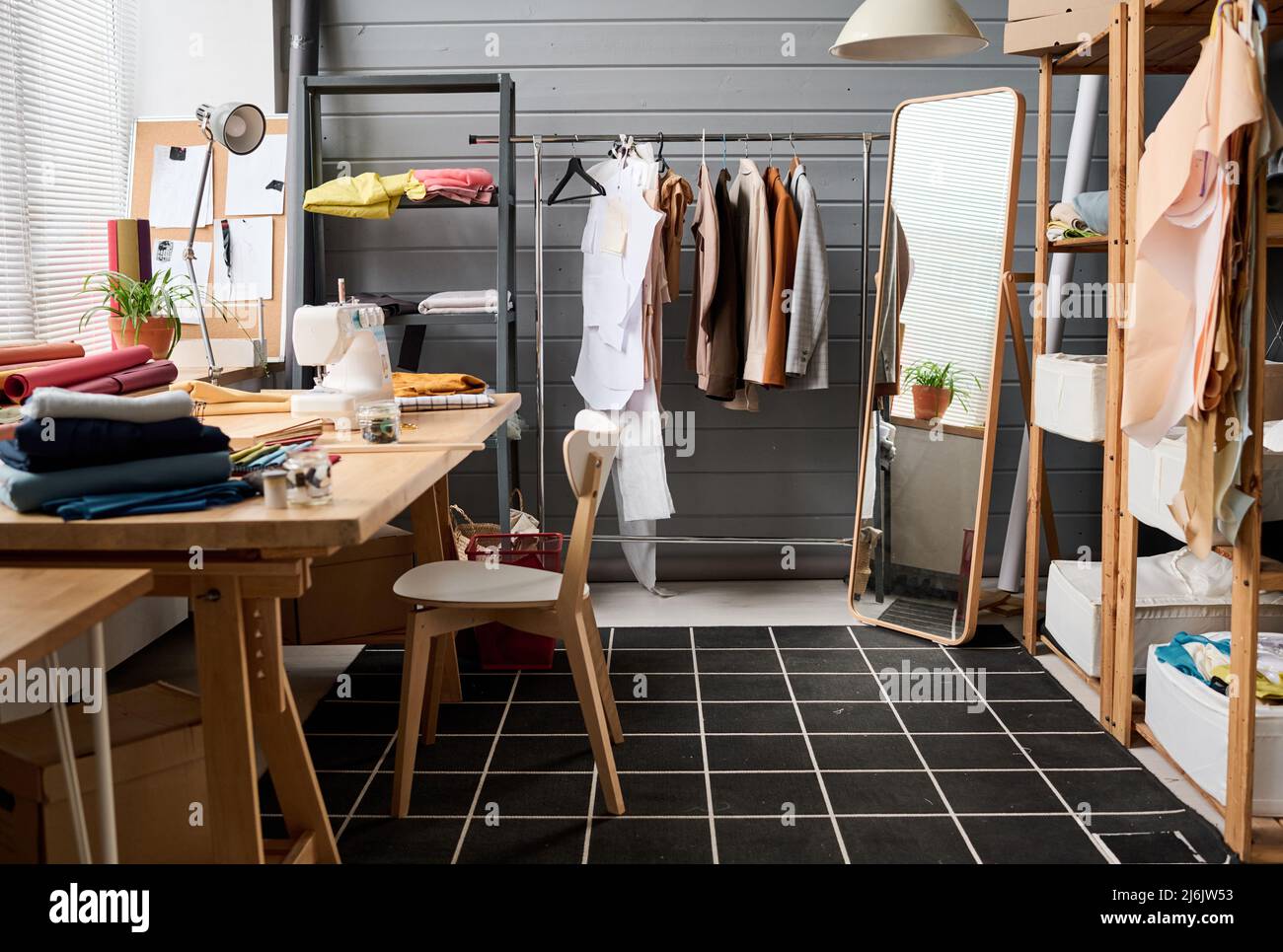 Intérieur de l'atelier spacieux de designer de mode moderne avec grand miroir, étagères, textile plié et machine à coudre sur table Banque D'Images