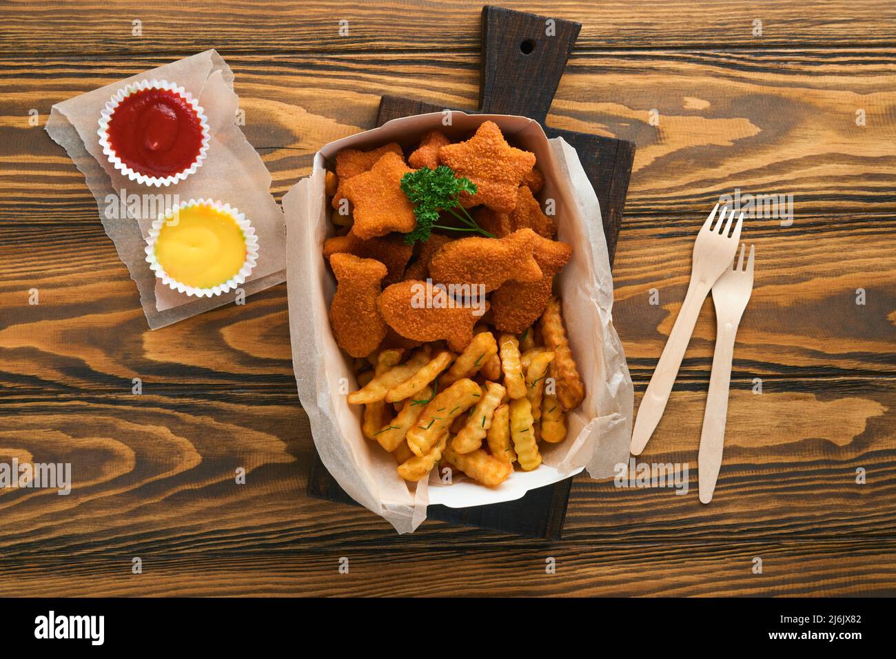 Fish and Chips, restauration rapide britannique. Bâtonnets de poisson avec frites sur une assiette en papier à emporter sur un fond de table en bois. Traditionnel anglais Banque D'Images