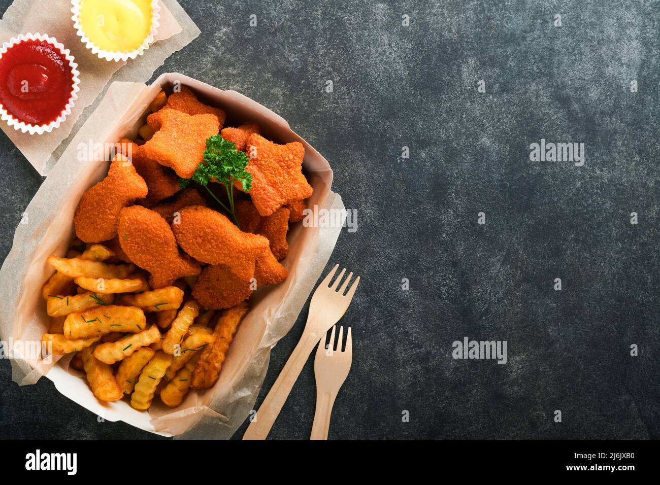 Fish and Chips, restauration rapide britannique. Bâtonnets de poisson avec frites sur une plaque de papier à emporter sur fond de béton ancien sombre. Traditionnel anglais authe Banque D'Images
