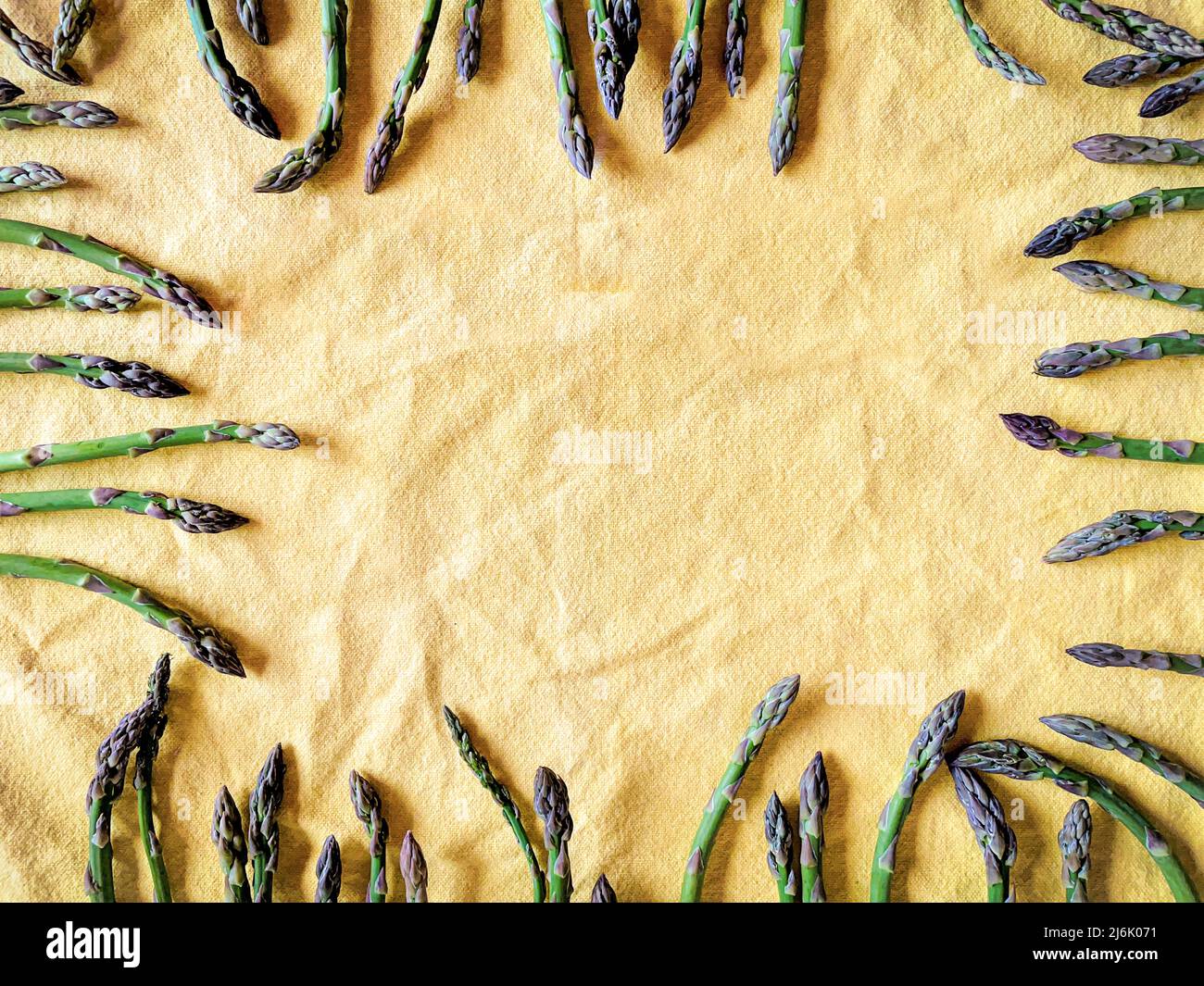 Asperges vertes fraîches cadre alimentaire autour de l'arrière-plan textile jaune avec espace pour le texte. Vue de dessus. Banque D'Images