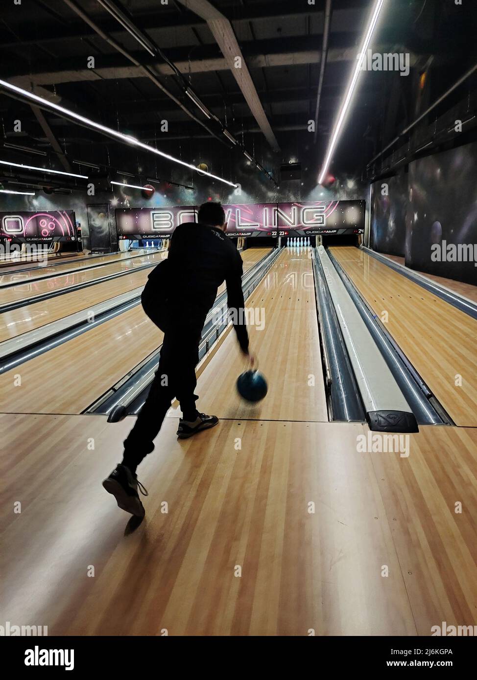 Guy adolescent joue au bowling, balance et jette le ballon dans les quilles. Vue arrière en perspective Banque D'Images