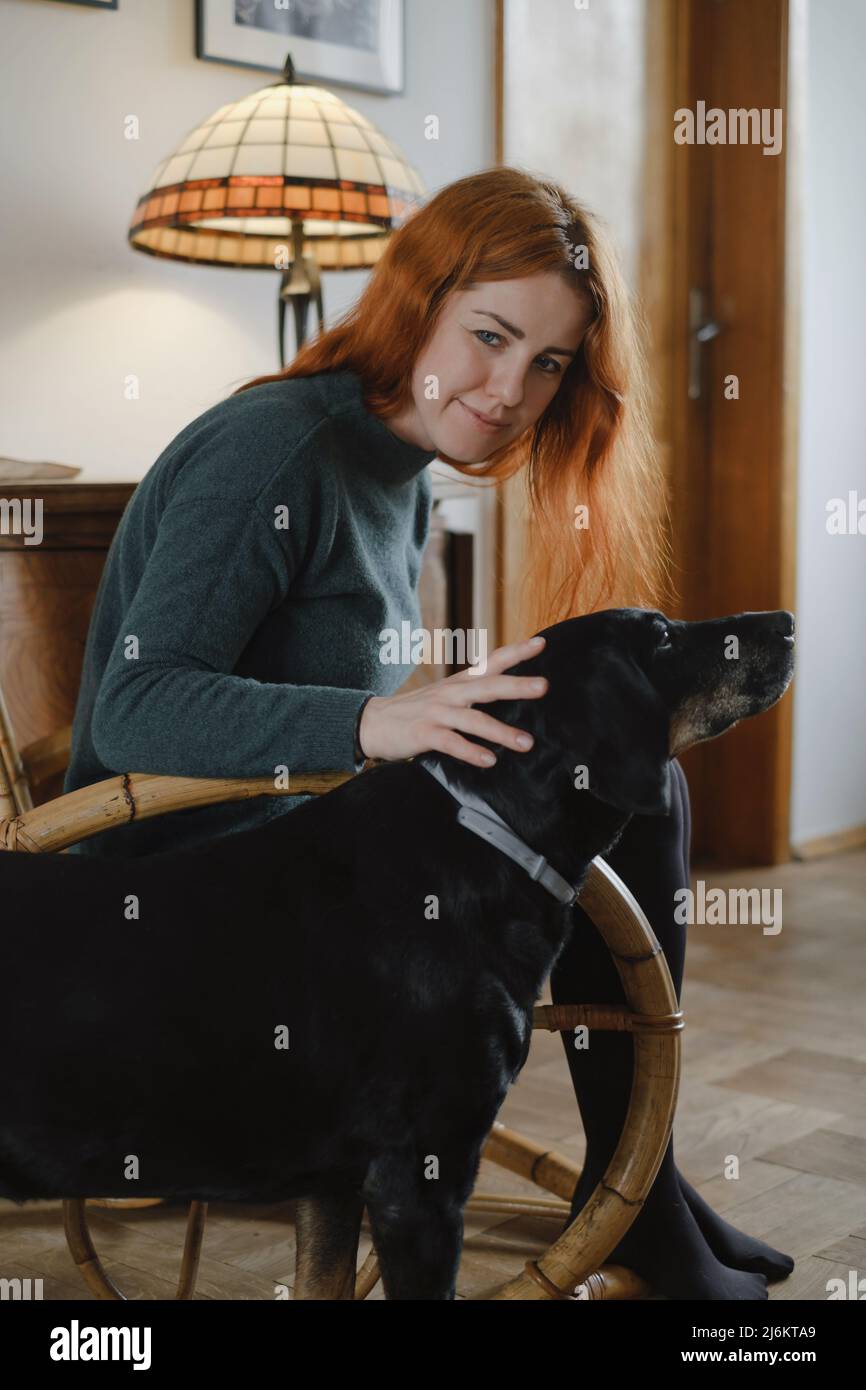 Femme sur une chaise à bascule qui a un gros chien noir. Ambiance décontractée. Maison d'époque pour la vie lente. Femme à son 40s repos. Banque D'Images