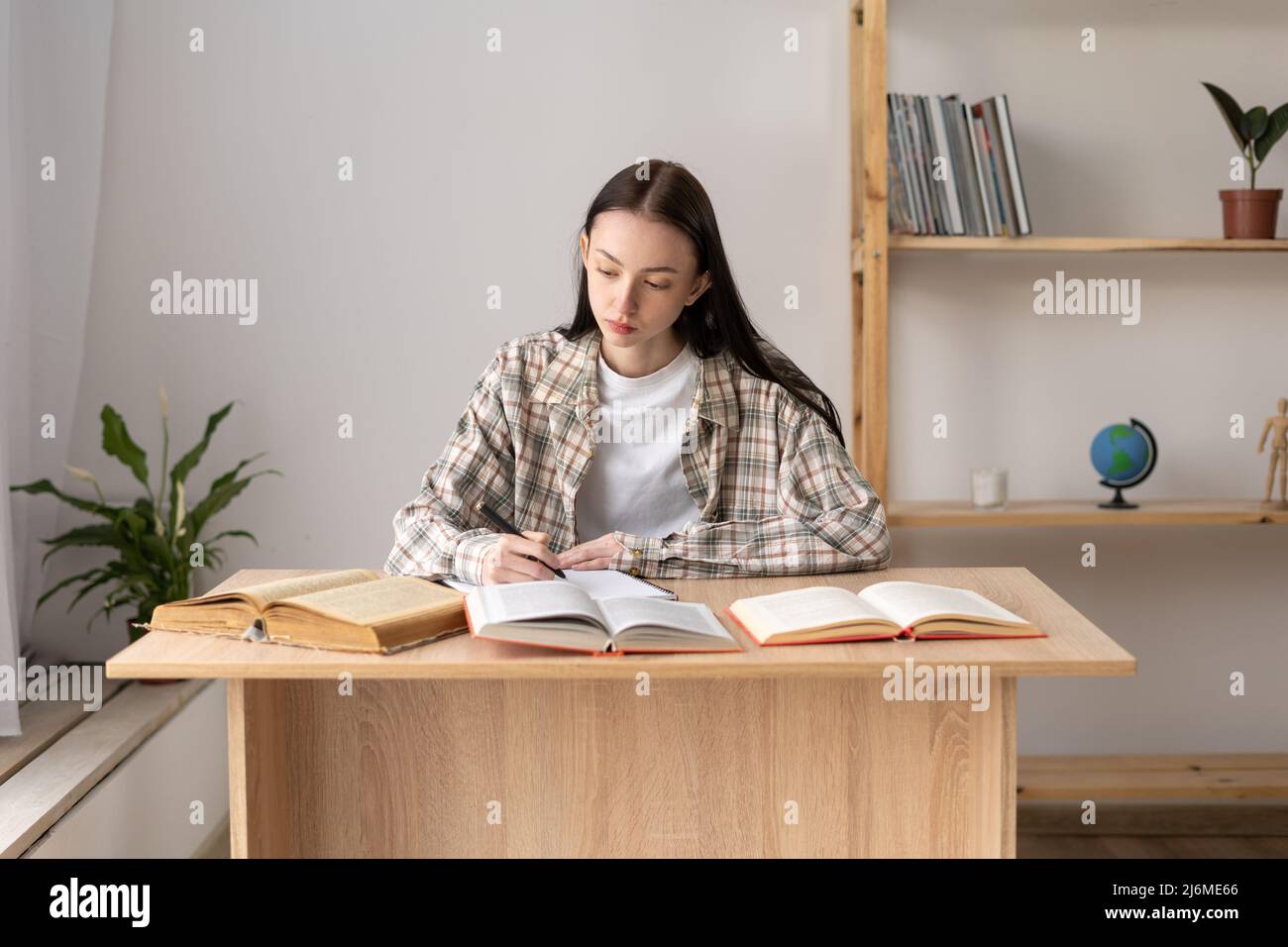 Enseignement à distance, jeune fille étudiant à la maison faire des devoirs en utilisant beaucoup de livres, étudier un sujet scolaire, préparer un projet de biologie, à la maison Banque D'Images