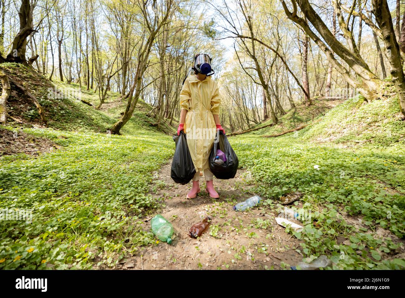 Femme en masque à gaz et vêtements de protection collectant les déchets de plastique éparpillés dans les bois Banque D'Images