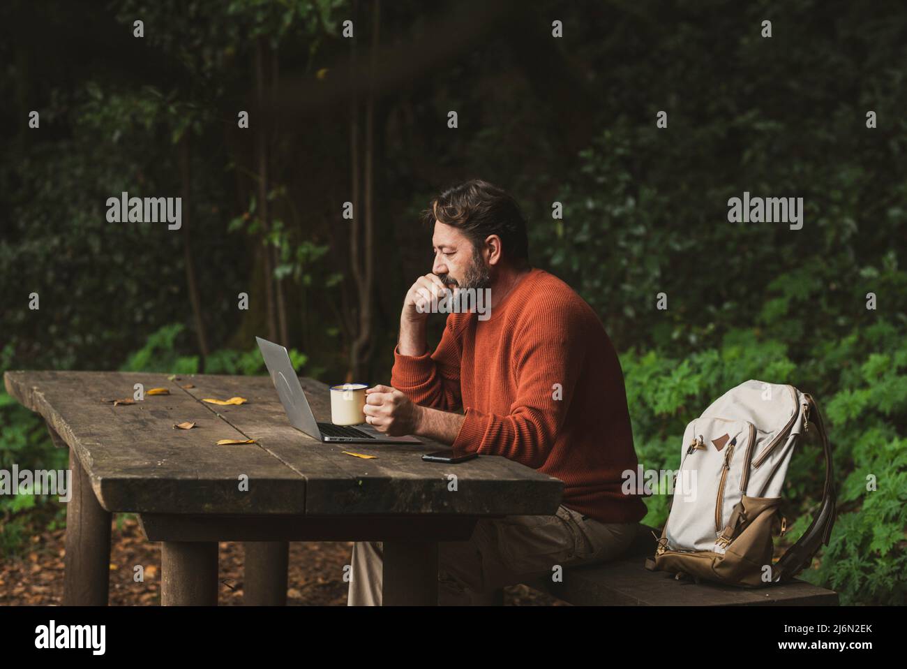 Un ouvrier mature s'assoit sur un banc en bois et travaille sur la table au milieu du parc, à l'extérieur des bois forestiers seuls. Sac à dos et ordinateur portable Banque D'Images