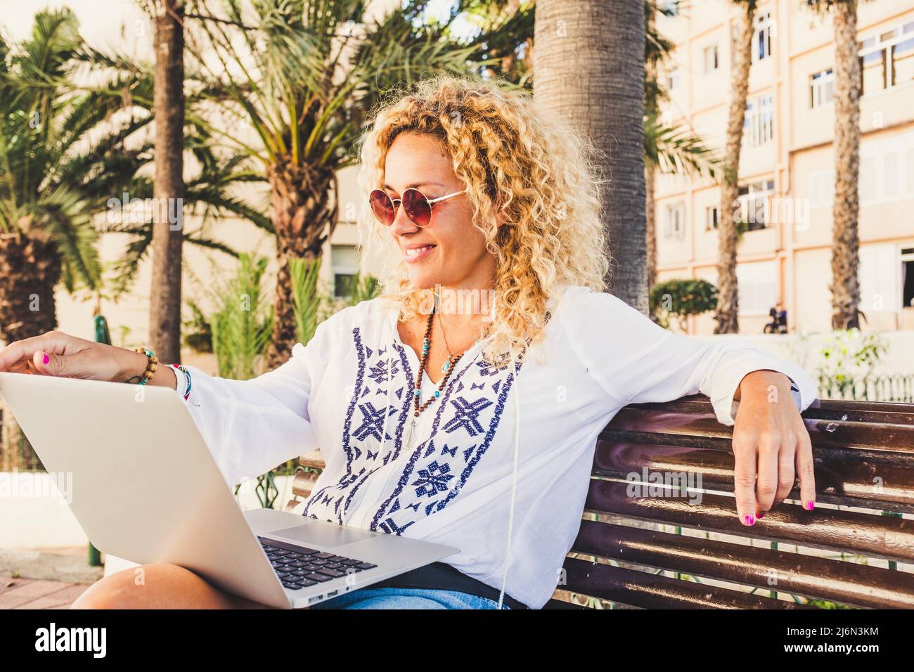 Gaie jolie femme adulte de travail et d'utiliser ordinateur portable à l'extérieur au parc assis sur un banc profitant de la liberté et de la connexion Internet gratuite - Banque D'Images