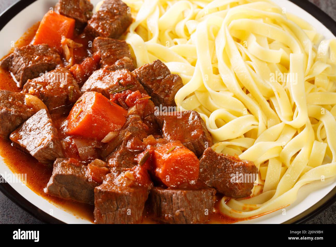 Mijoté de bœuf épicé dans du vin rouge avec des légumes servis avec des nouilles dans une assiette sur la table. Horizontale Banque D'Images
