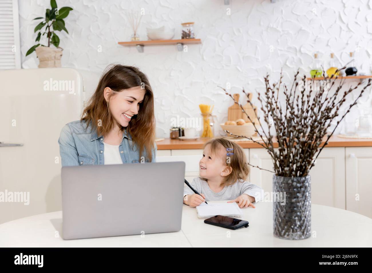 Jeune mère célibataire assise au bureau avec un enfant mignon, travaillant à distance de la maison. Jeune femme d'affaires en congé de maternité avec ordinateur portable Banque D'Images