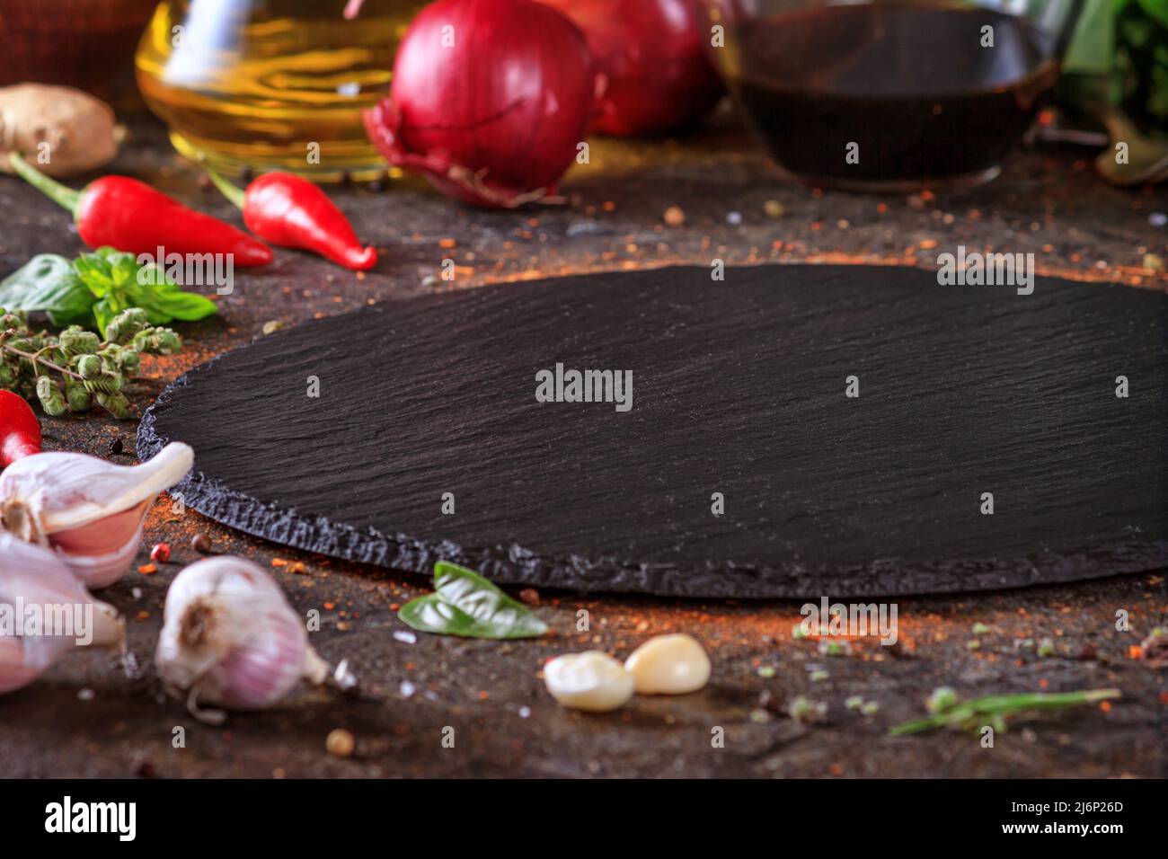 Décor culinaire avec table ronde en ardoise, huile d'olive dans une carafe et légumes.Espace vide pour le menu ou la recette avec mise au point sélective Banque D'Images