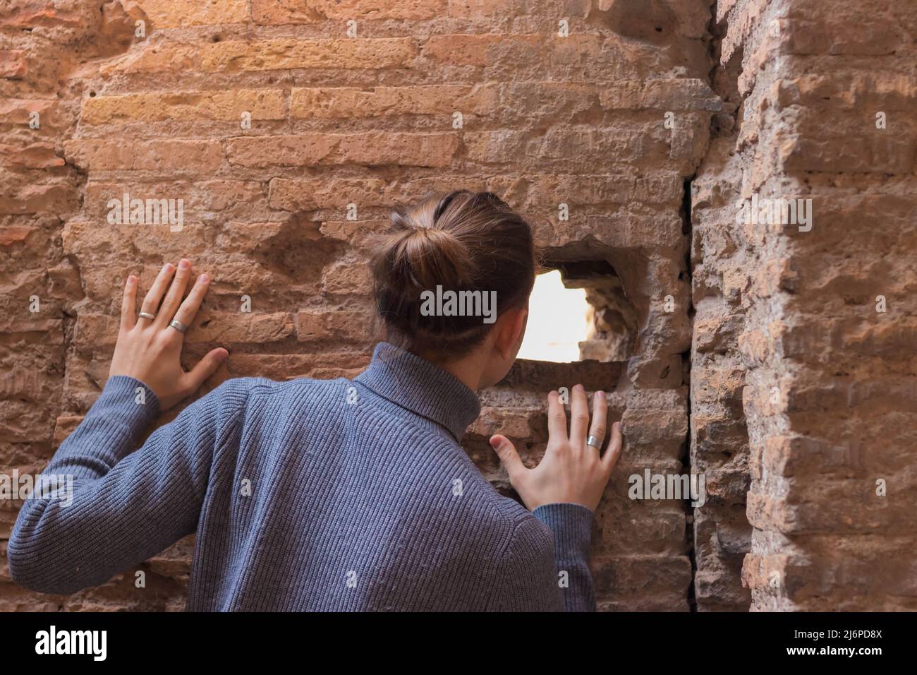 Le jeune homme en arrière avec un petit pain dans ses cheveux peeking curieusement à travers le creux de la ruine historique de brique Banque D'Images