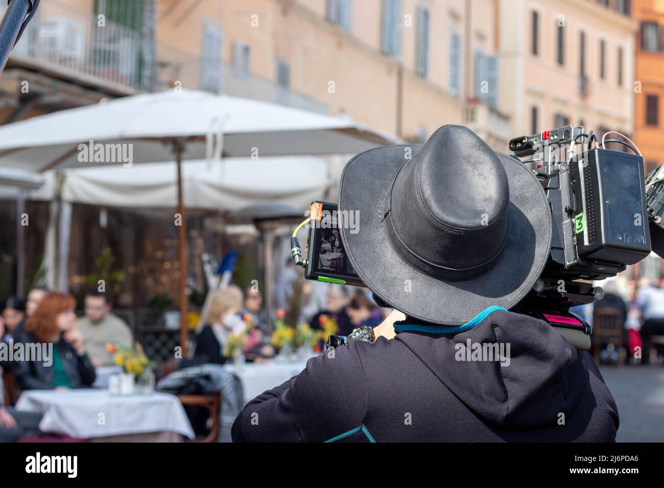 Rome, Italie - 17th mars 2022. Journaliste de nouvelles avec caméra et chapeau enregistrement en direct pour des nouvelles en Italie aux personnes qui mangent et boire dans la terrasse Banque D'Images