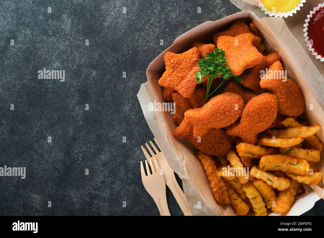 Fish and Chips, restauration rapide britannique. Bâtonnets de poisson avec frites sur une plaque de papier à emporter sur fond de béton ancien sombre. Traditionnel anglais authe Banque D'Images