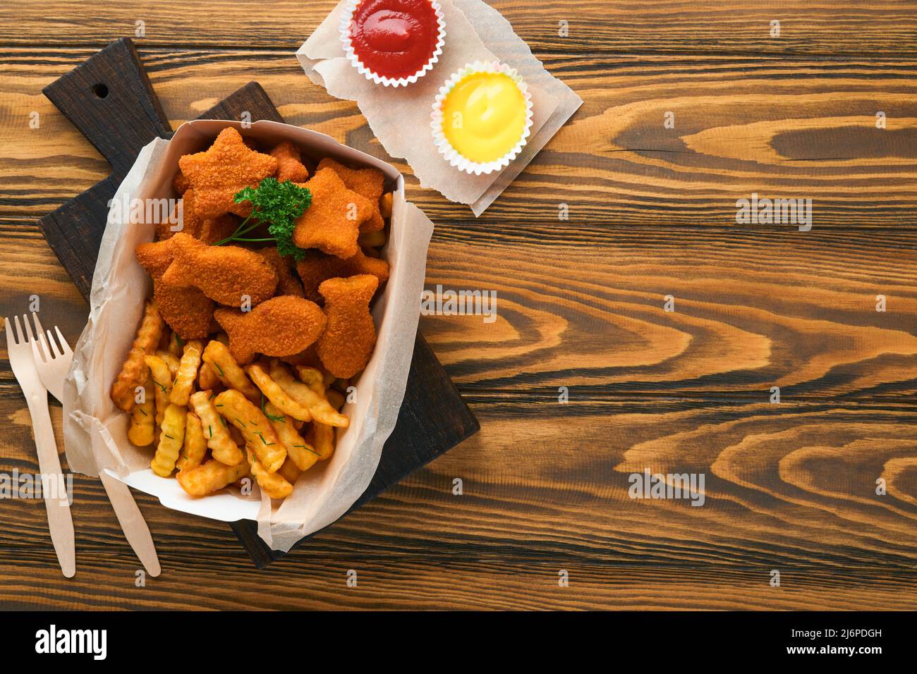 Fish and Chips, restauration rapide britannique. Bâtonnets de poisson avec frites sur une assiette en papier à emporter sur un fond de table en bois. Traditionnel anglais Banque D'Images