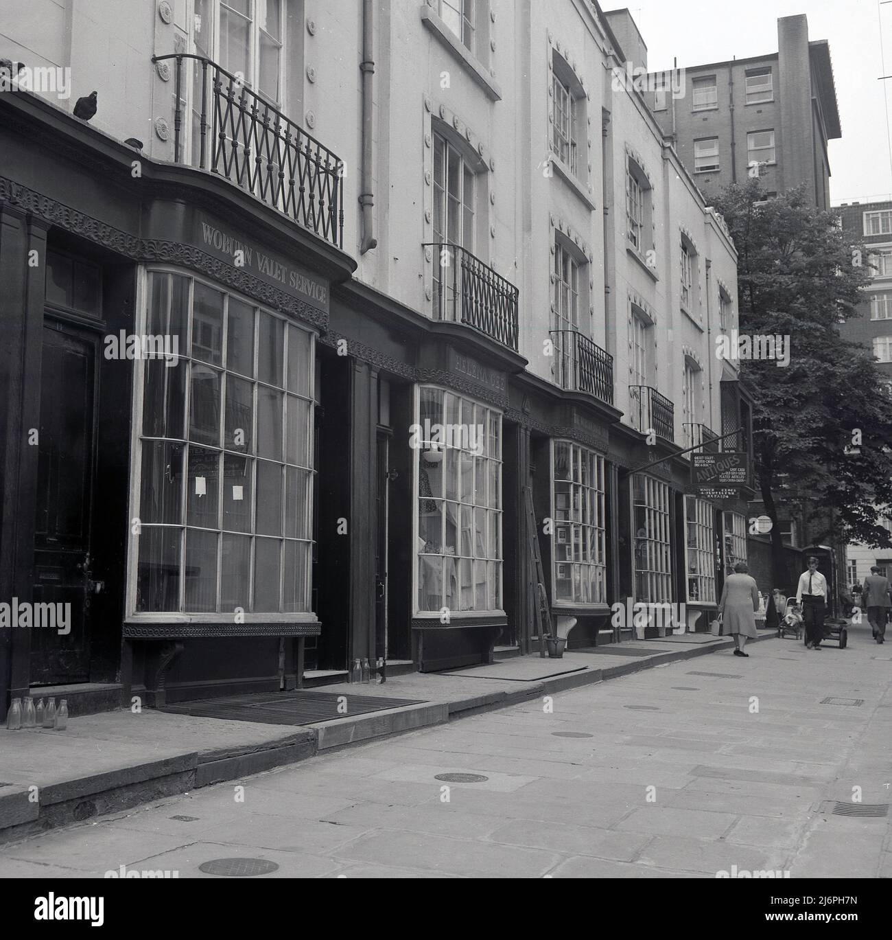 1960s, historique, Woburn Walk, Bloomsbury, Londres, Angleterre, Royaume-Uni. On voit sur l'image le Woburn Valet Service et Helena Gee. Une rue piétonne commerçante, son nom est dérivé de l'abbaye de Woburn, le siège anglais des Ducs de Bedford, qui possédaient et développa la région. Conçu par Thomas Cubitt en 1822, il s'agissait de la première rue commerçante piétonne de Londres. Les façades de magasins ont une apparence distinctive, avec les fenêtres composées de petits panneaux individuels de verre et étant Dickensian Bow-fronted dans le style. Banque D'Images