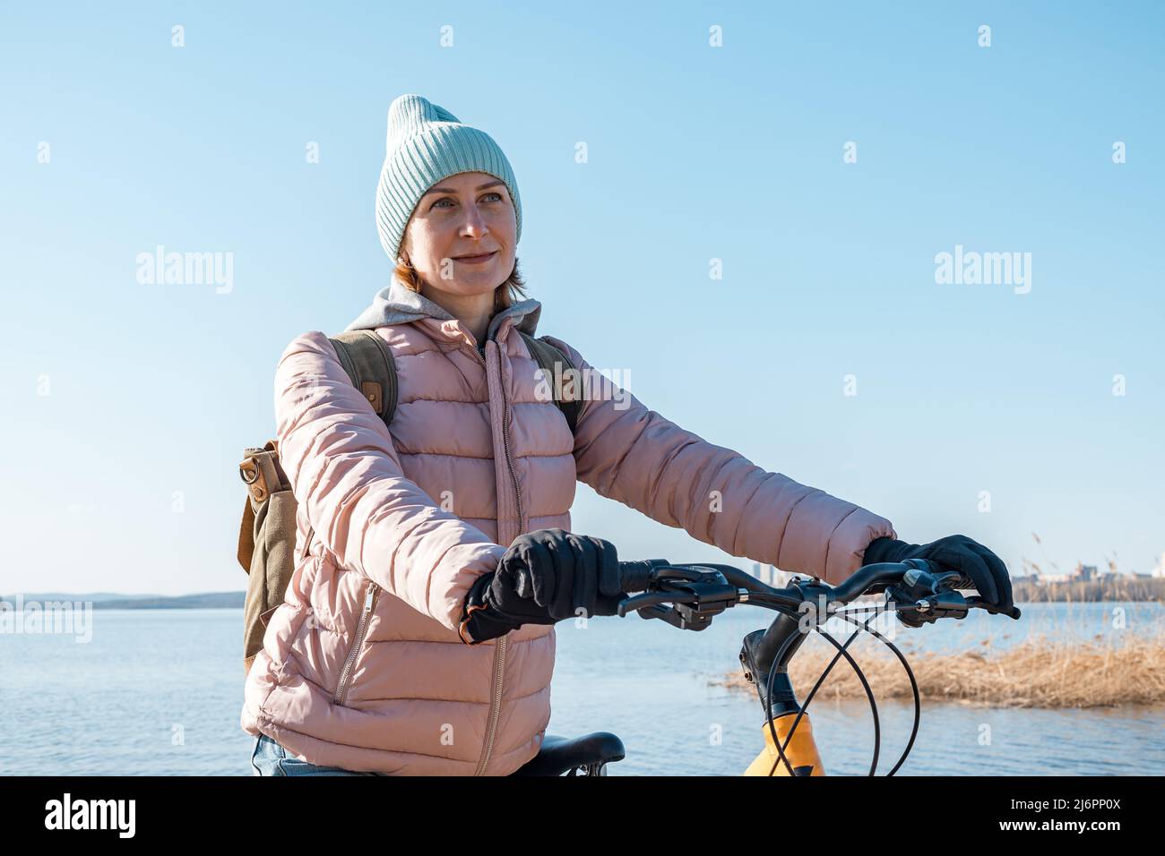 Une jeune femme est debout avec un vélo. Promenez-vous à l'extérieur. En regardant sur le côté. Jolie jeune femme d'origine caucasienne avec un sac à dos et une chaude cl Banque D'Images