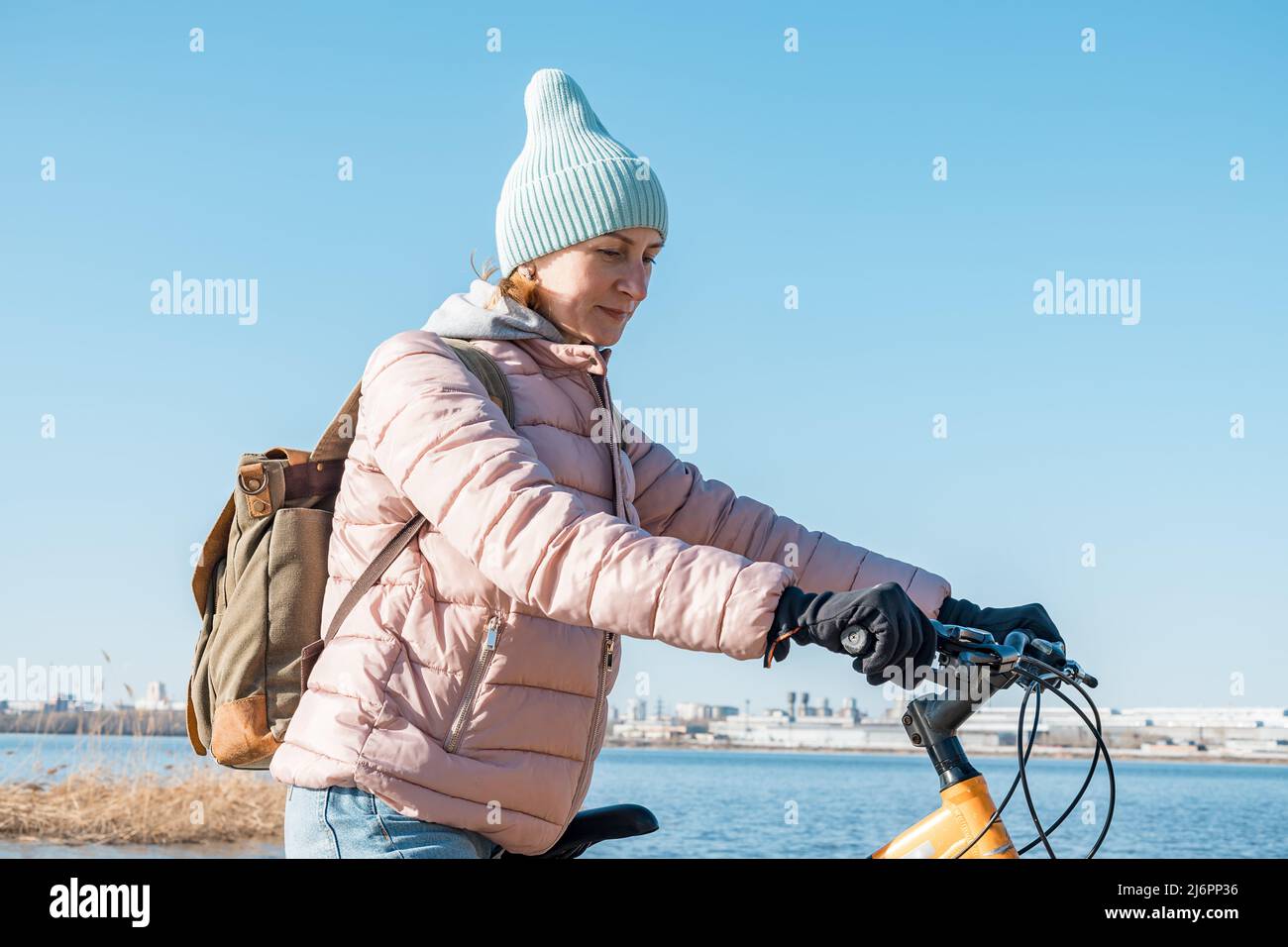 Une jeune femme est debout avec un vélo. Promenez-vous à l'extérieur. En regardant sur le côté. Jolie jeune femme d'origine caucasienne avec un sac à dos et chaude Banque D'Images