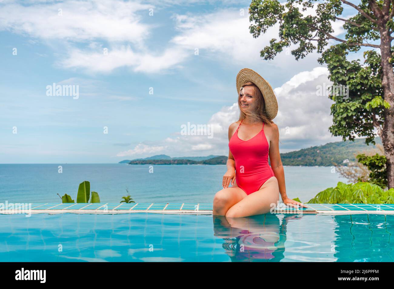 Jeune femme sensuelle en maillot de bain et chapeau de paille se détendre dans la piscine bleue Banque D'Images