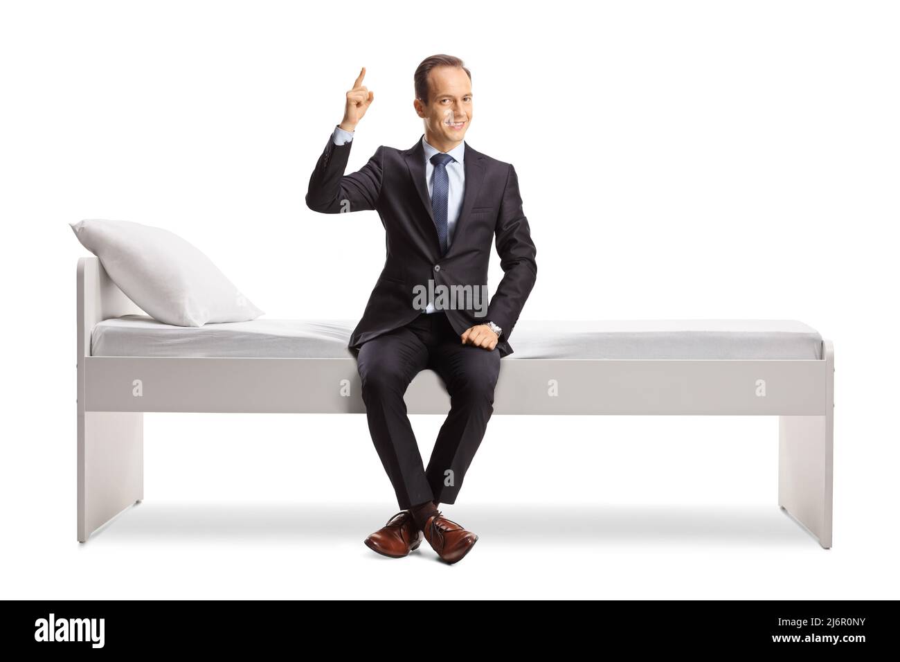 Homme d'affaires assis sur un lit et pointant vers le haut isolé sur fond blanc Banque D'Images