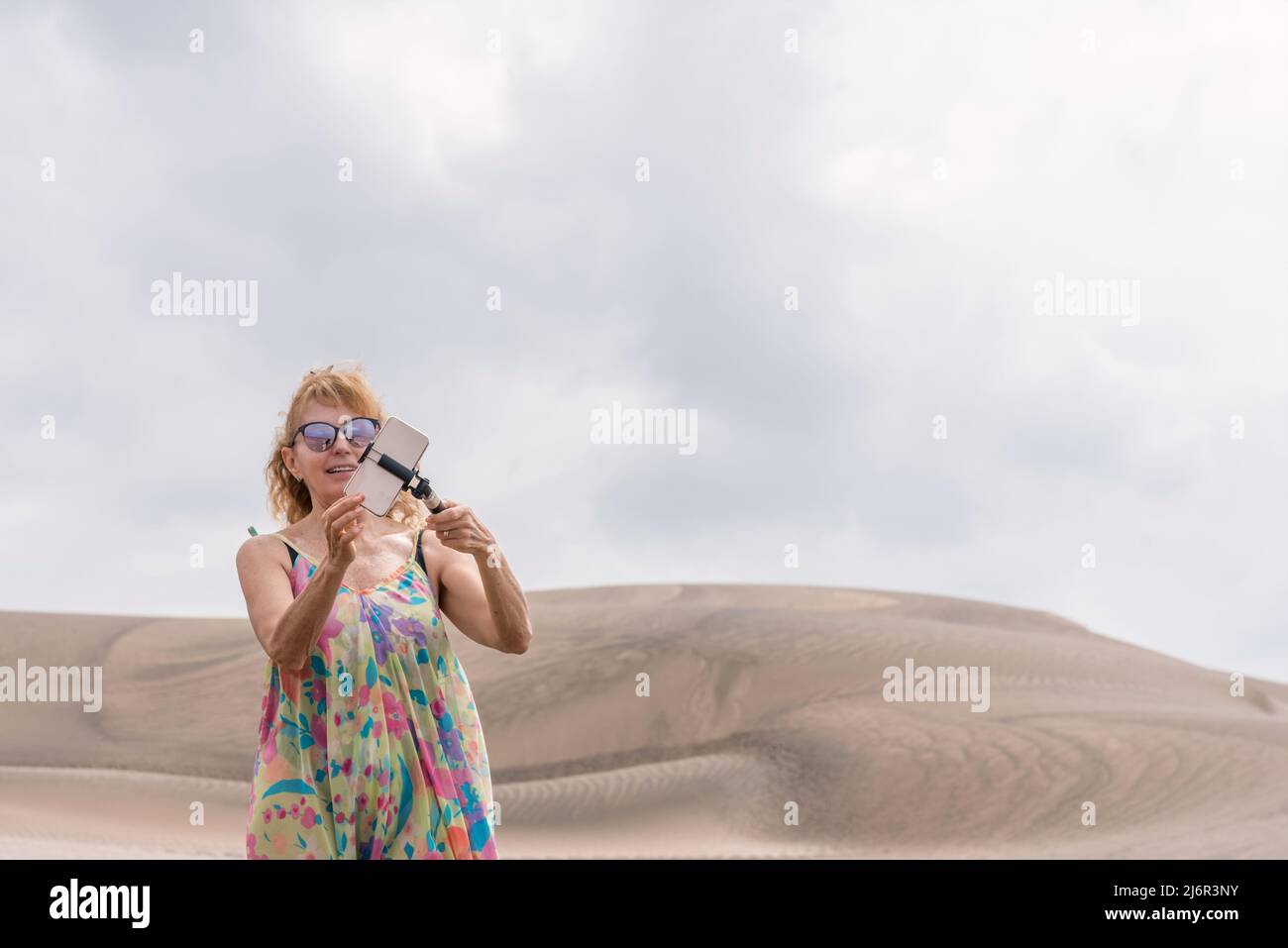 Femme blonde en robe faisant un selfie avec le mobile au milieu des dunes Banque D'Images