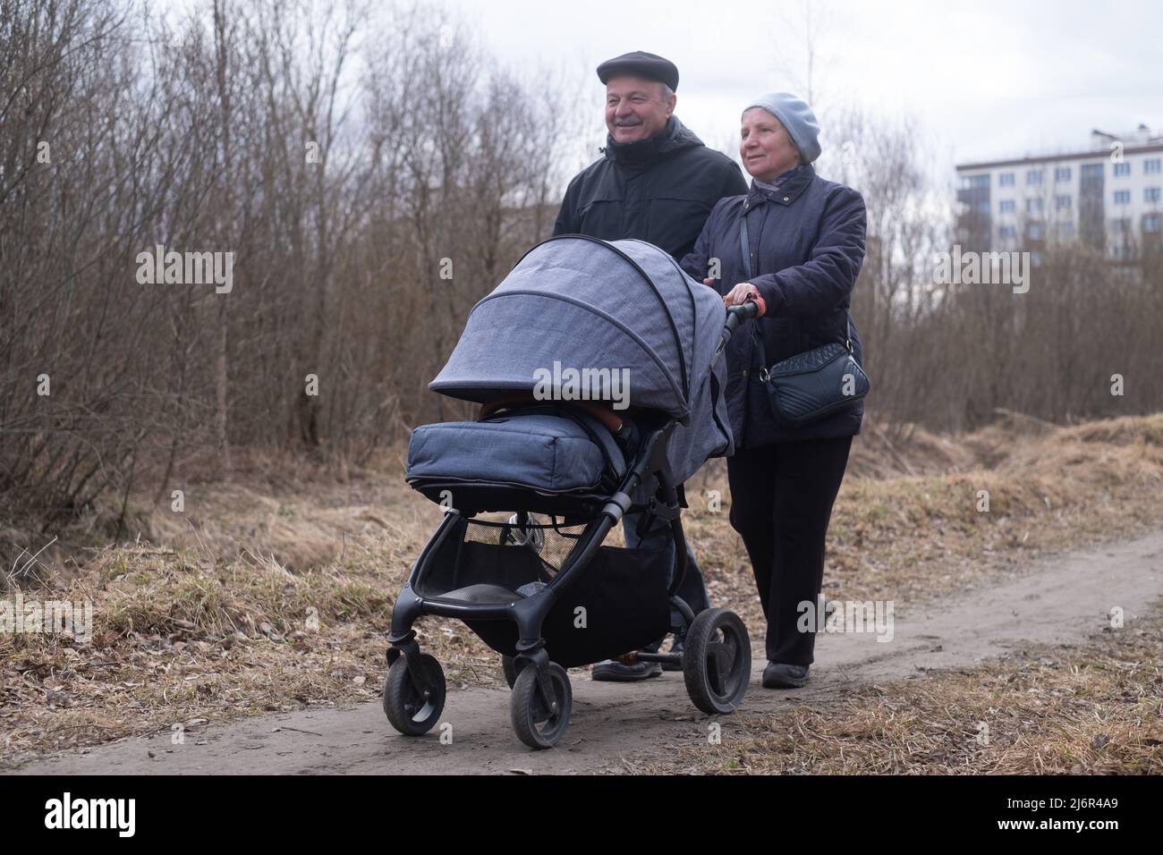 Heureux grands-parents marchant avec une poussette dans le parc au début du printemps. Banque D'Images