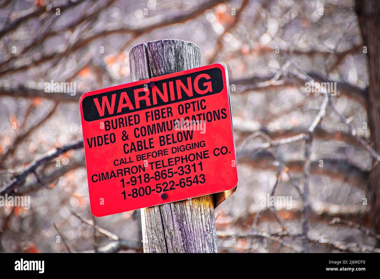 3-16-2022 Osage Co. OK USA - panneau rouge affiché sur le poteau lit avertissement câble en fibre optique enterré - arrière-plan bokeh des arbres d'hiver - gros plan Banque D'Images