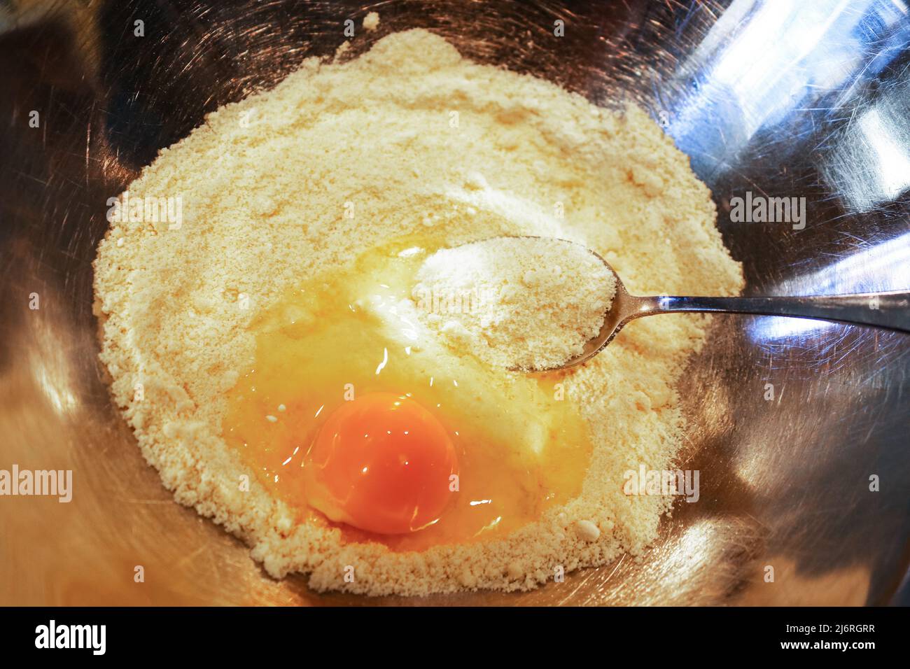 Cuisson basse teneur en glucides sans gluten - un œuf brisé en une pile de farine d'amande avec une cuillère prête à l'incorporer dans un bol en acier inoxydable - gros plan Banque D'Images