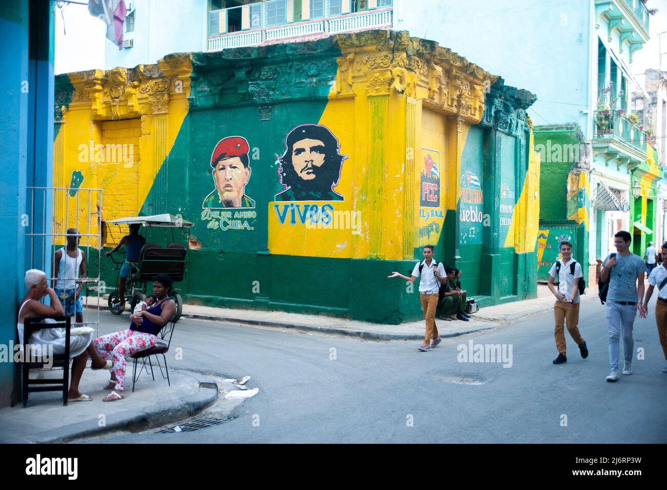 Les garçons de l'école cubaine marchent dans un coin de rue près des images de Hugo Chávez et Che dans la Vieille Havane, Cuba passé une jeune mère tenant son nouveau-né. Banque D'Images