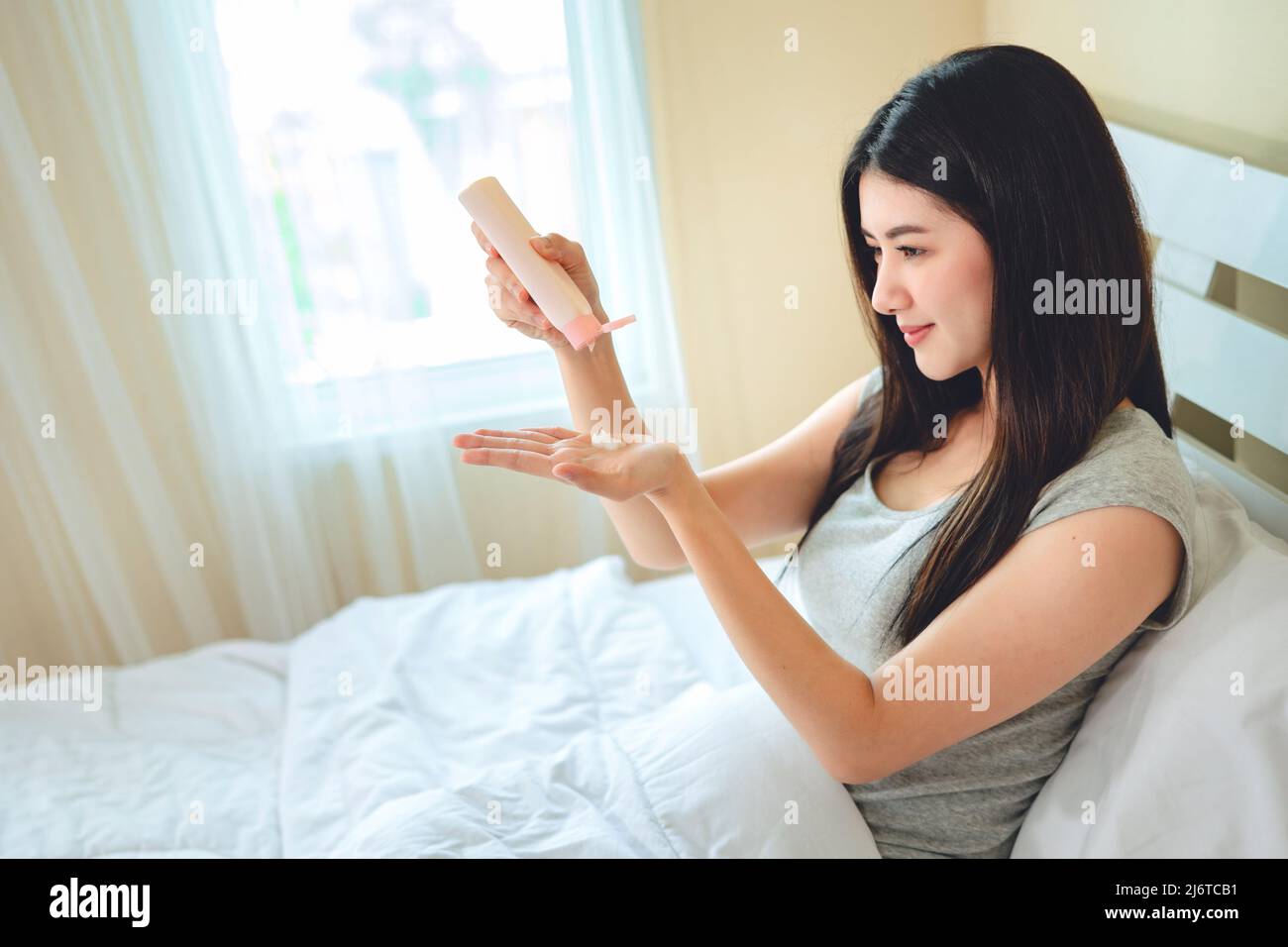 femme asiatique utiliser lotion mains crème humidité et crème hydratante blanche sur le lit dans la chambre, beauté thérapeutique, concept de soins de la peau. Banque D'Images