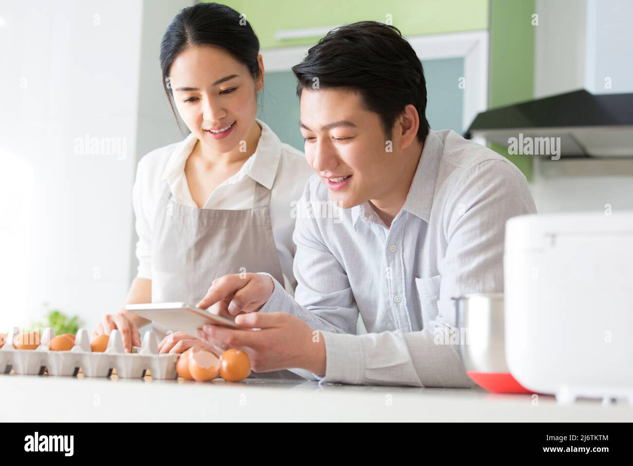 Dans la cuisine familiale, un jeune couple aime cuisiner ensemble. Ils utilisent des tablettes pour regarder la planification financière - photo de stock Banque D'Images
