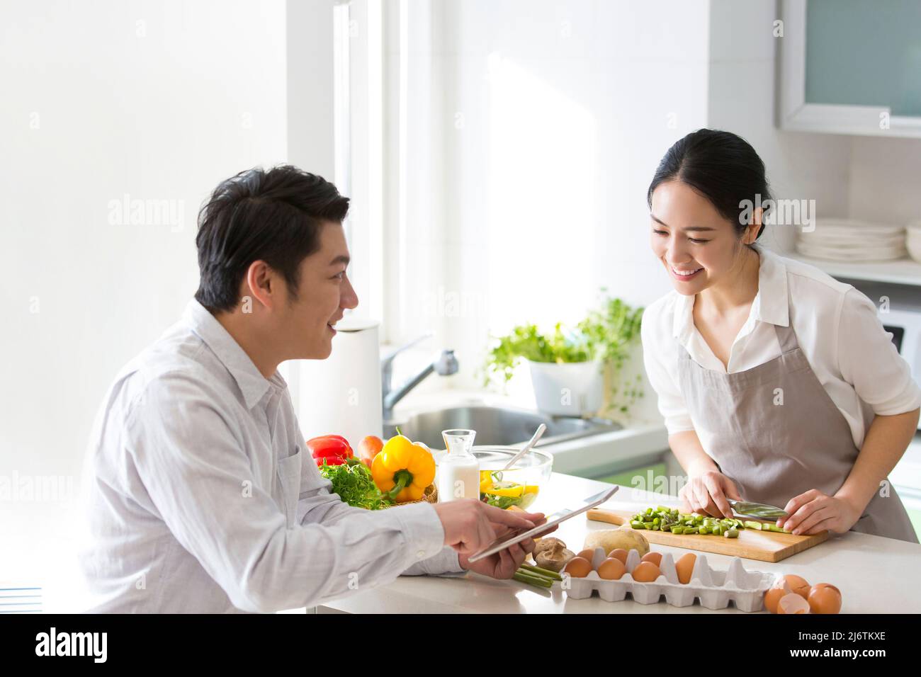 Dans la cuisine familiale, un jeune couple aime cuisiner ensemble. Ils utilisent des tablettes pour regarder la planification financière - photo de stock Banque D'Images
