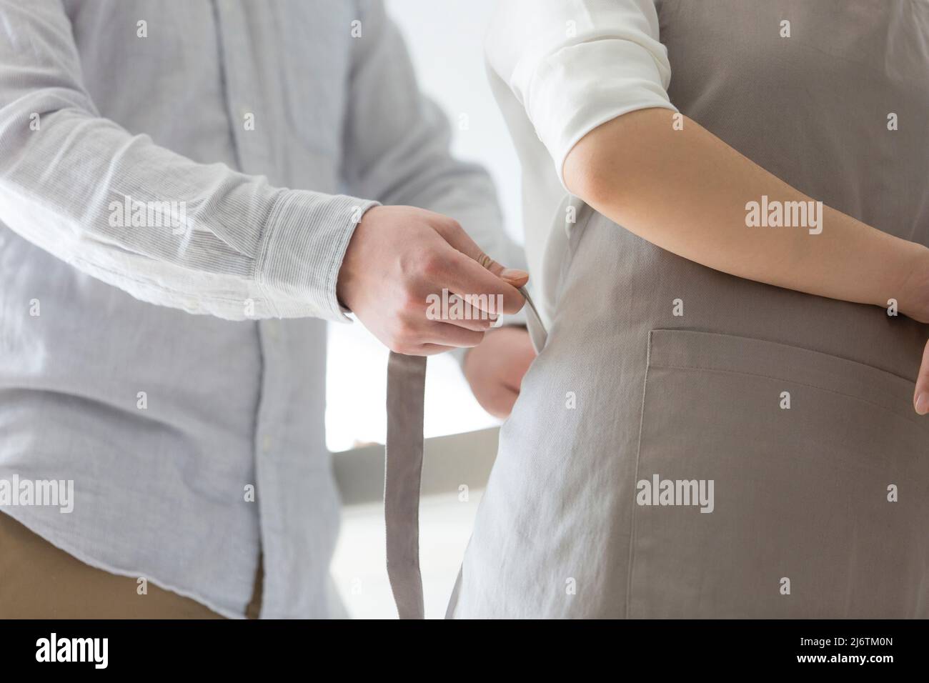 Dans la cuisine familiale, un jeune couple de jeunes mariés aime cuisiner ensemble. Gros plan du mari aidant la femme à attacher un tablier - photo de stock Banque D'Images