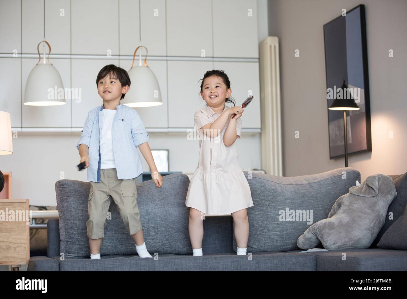 Une petite fille et un petit garçon chantant sur le canapé avec un peigne agissant comme un microphone - photo de stock Banque D'Images