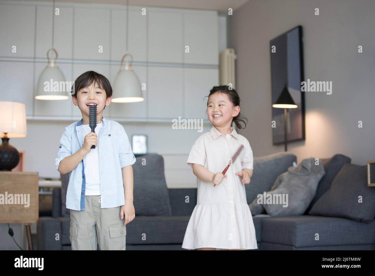 Une petite fille et un petit garçon chantant avec un peigne comme microphone dans le salon - photo de stock Banque D'Images
