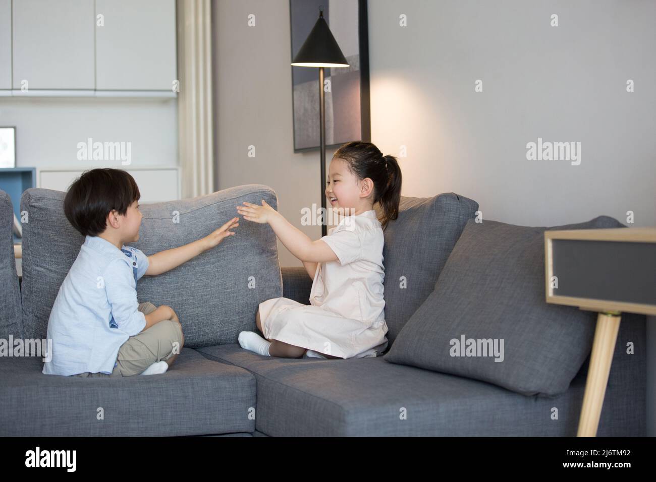 Une petite fille et un petit garçon jouent main clapping sur le canapé du salon - photo de stock Banque D'Images