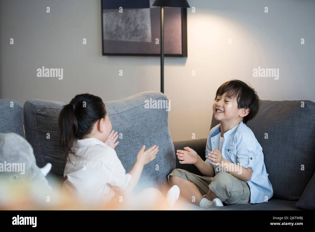 Une petite fille et un petit garçon jouent main clapping sur le canapé du salon - photo de stock Banque D'Images