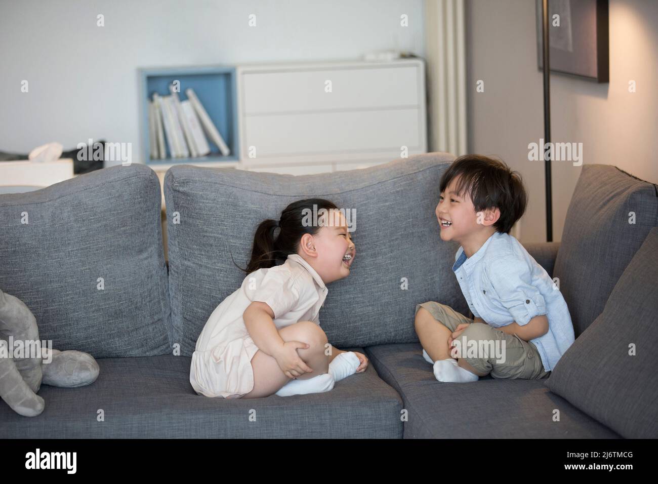 Une petite fille et un petit garçon assis sur le canapé du salon riant - photo de stock Banque D'Images