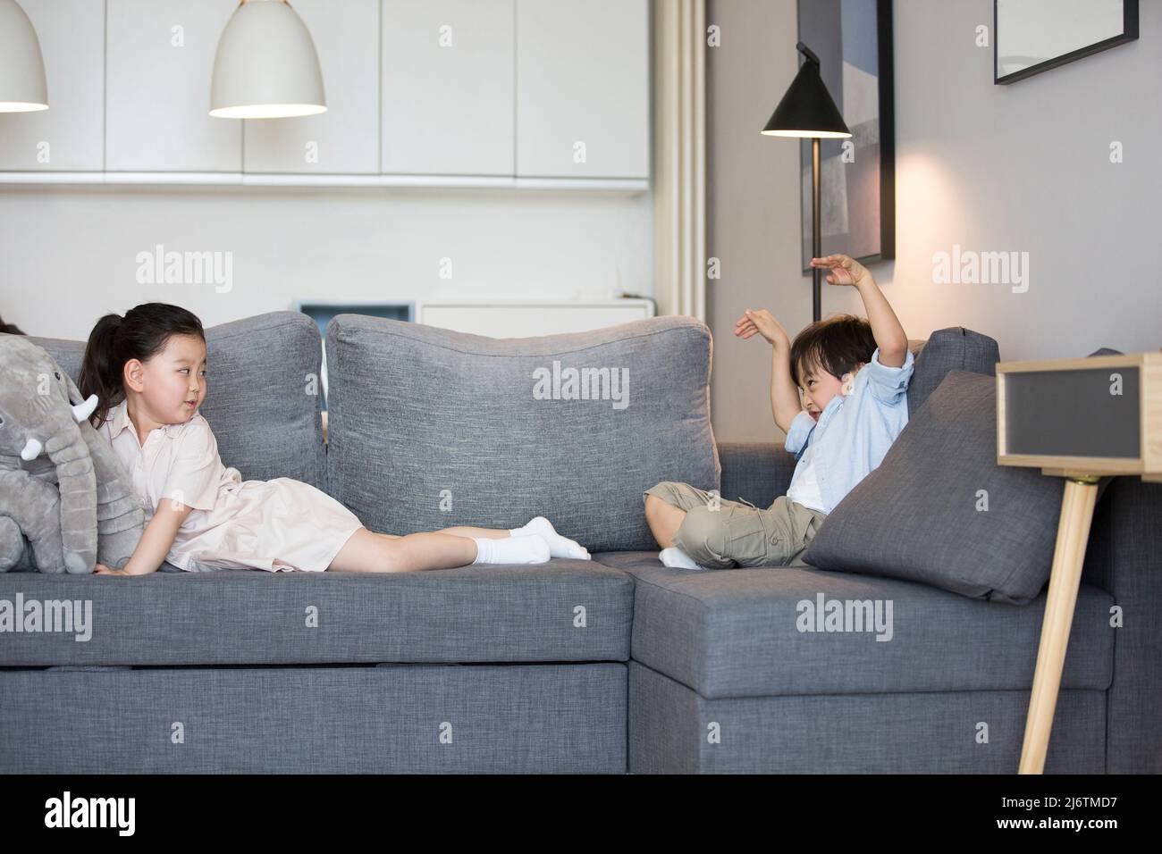 Une petite fille et un petit garçon assis sur le canapé dans le salon jouant un jeu - photo de stock Banque D'Images
