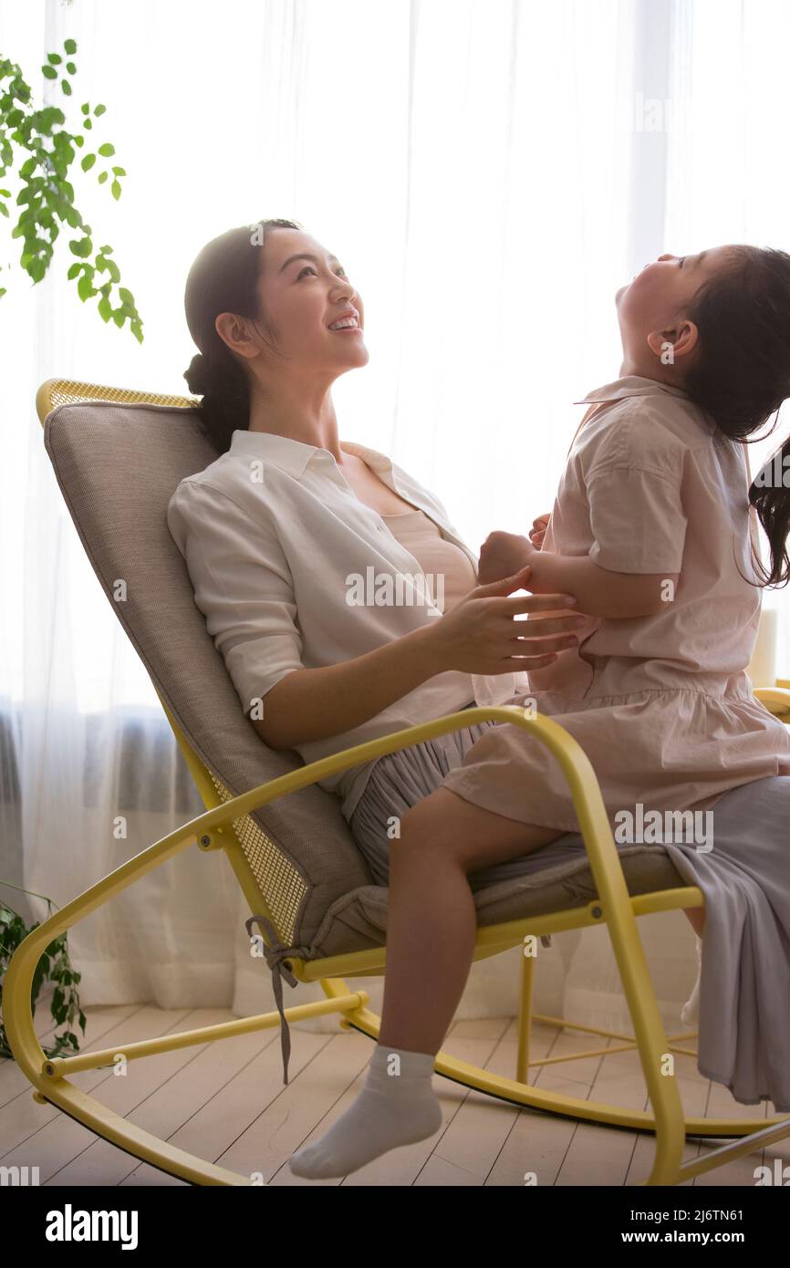 Une petite fille s'assoit sur les genoux de sa jeune mère alors qu'elle secoue la chaise à bascule et chante les chansons des enfants et raconte des contes de fées - photo de stock Banque D'Images