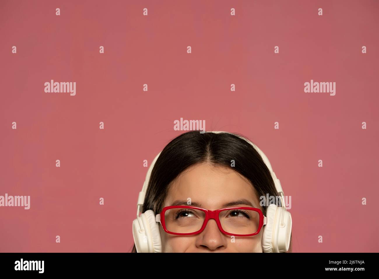 Un demi-portrait d'une belle femme heureuse dans un casque blanc écoute de la musique sur fond rose Banque D'Images