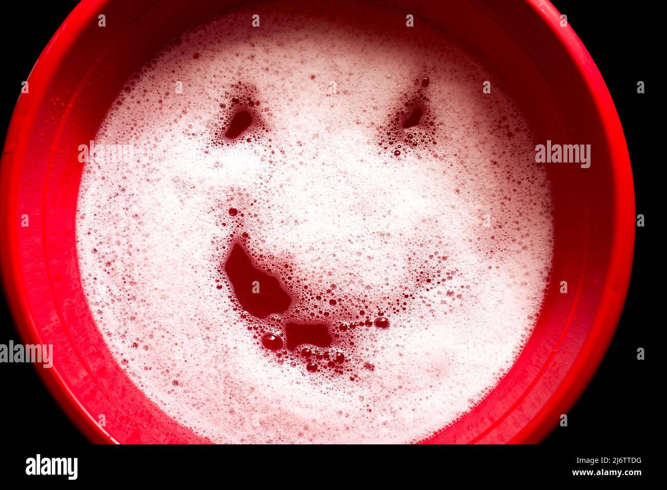 Bassin en plastique rouge avec un visage emoji sur la surface de l'eau. Mousse blanche avec visage souriant. Banque D'Images