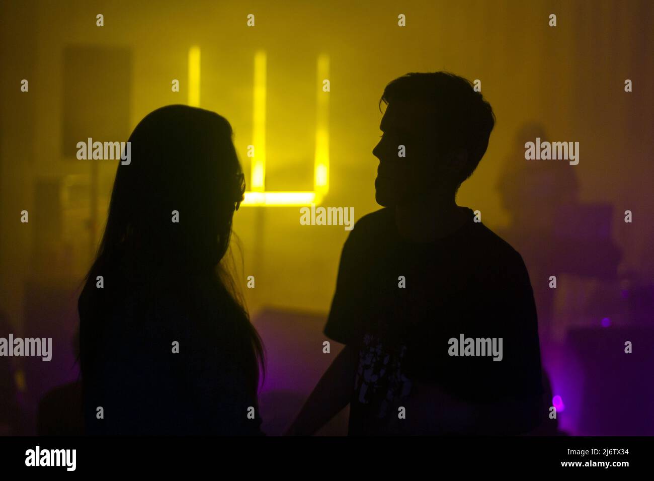 Une silhouette d'un jeune couple lors d'un concert dans une lumière ambiante sombre jaune et violette Banque D'Images